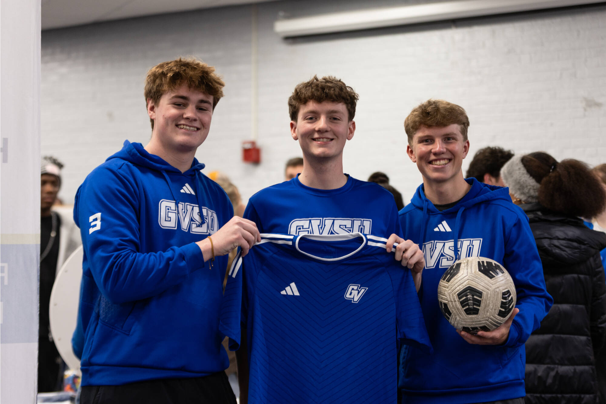 3 men's soccer players smiling with a jersey and ball
